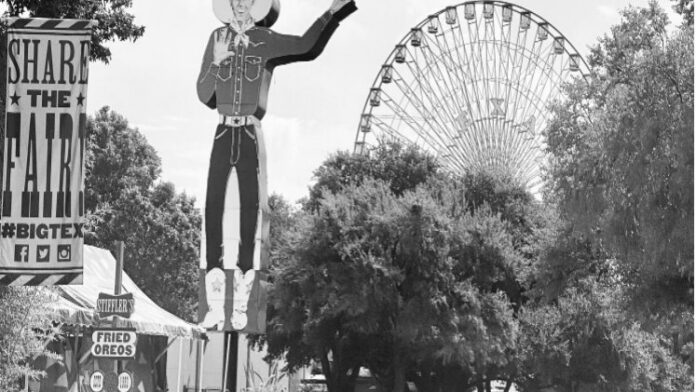 Statue of a cowboy with raised arm, with a Ferris wheel visible in the background.
