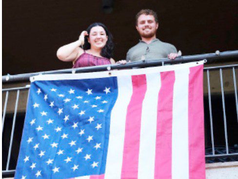Adriana Terrazas and Mike Miller hold up an American flag while announcing the 2026 Charity Week theme
