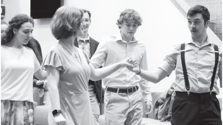 Five people in formal attire holding hands in a line during a dance formation.