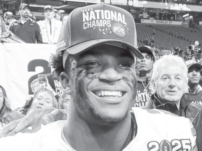 caleb-downs-a-new-legacy-in-dallas-1 Caleb Downs smiles while wearing a National Champs cap in a stadium setting.