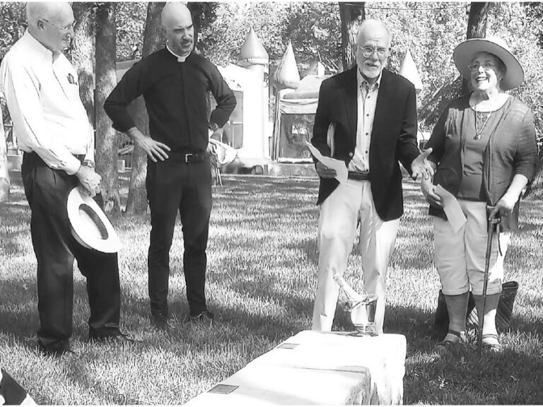 People in formal attire stand on a church lawn during a dedication ceremony.