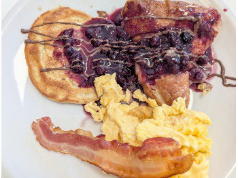 due-santis-new-chef-1 A plate with scrambled eggs, bacon, sliced meat, and a pastry.