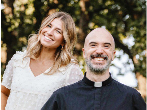 Madison Brinkman and Fr. Jeronimo smile outdoors with trees in the background.