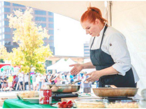 italian-culture-finds-a-home-in-las-colinas-1 A person in an apron preparing Italian food at an outdoor cooking station with festival attendees visible in the background.