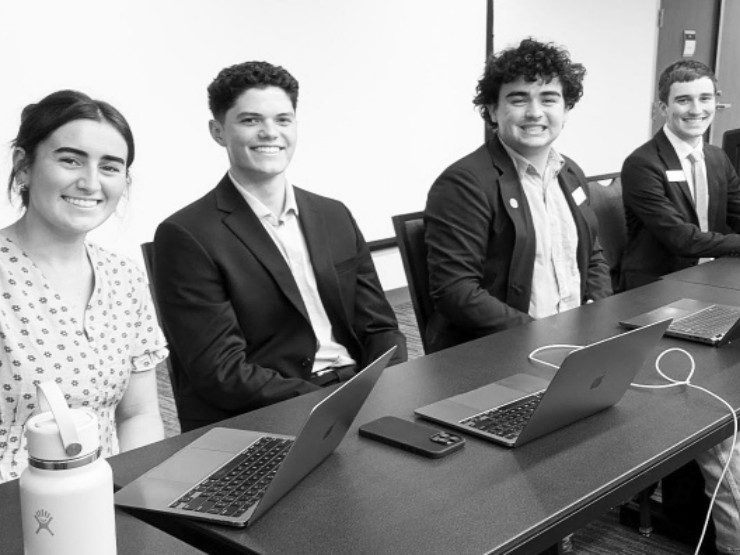 Four student government members seated at a table with laptops during a meeting.