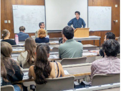Students sit in a lecture hall, viewing a debate about Islam and religious freedom.